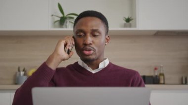 Satış müdürü, oturma odasındaki uzak işinden bir dizüstü bilgisayarın önünde telefonla konuşuyor.
