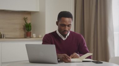 Genç Afrikalı Amerikalı adam faturalarını kontrol ediyor ve ev harcamalarını yönetiyor.