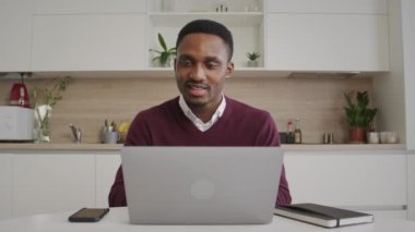 Afro-Amerikalı genç siyahi girişimci bilgisayarında çalışırken mutlu ve gülümsüyor.