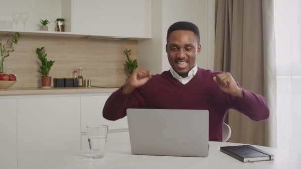 ユーフォリックな黒人男性学生は、仕事のオファーを得る試験に合格ノートパソコンの画面の悲鳴を見て机に座っています。アフリカ系アメリカ人の男は、コンピュータ上で楽しい電子メールメッセージを受信興奮を感じる — ストック動画