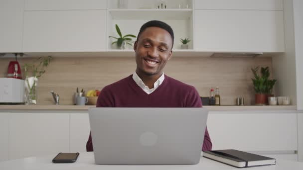 Happy smiling african american man greeting his friends on a video call on a laptop at home interior — Stock Video