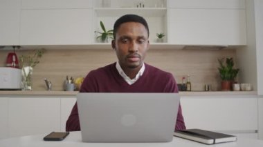 Odaklanmış Afro-Amerikan adam evinde dizüstü bilgisayara bakıyor.