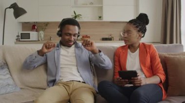 Afrikalı Amerikalı çift evlerinde müzik dinlerken kanepede oturup dans ediyorlar.