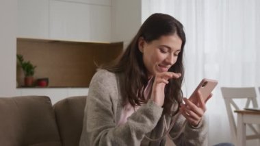 Genç beyaz kadın internette sosyal medyada gezinirken akıllı telefonuyla gülüyor ve süzülüyor.