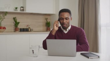 20 'li yaşlardaki Afro-Amerikan siyahi girişimci ev bilgisayarında çalışırken telefonla konuşuyor.