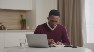Genç Afrikalı Amerikalı adam faturalarını kontrol ediyor ve ev harcamalarını yönetiyor.