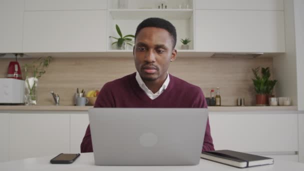 Afrikanischer junger schwarzer Unternehmer, der in seinem hellen Homeoffice glücklich und lächelnd an seinem Laptop arbeitet — Stockvideo