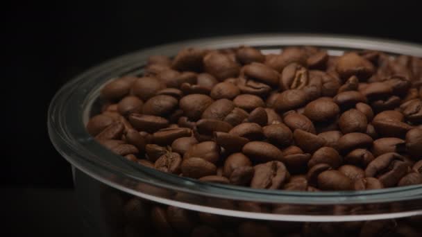 Cierre la bandeja de cámara lenta sobre una placa de vidrio llena de granos de café arábica aromáticos sobre un fondo oscuro — Vídeo de stock