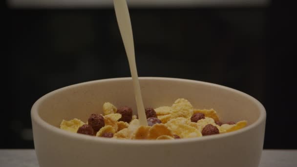 Melk gieten in een kom plaat gevuld met cornflakes op een zwarte achtergrond — Stockvideo