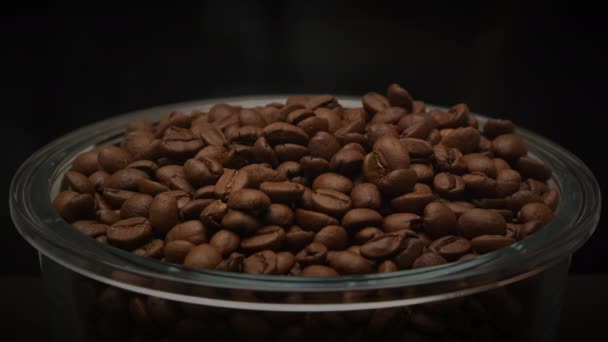 Aromatische gebrande koffiebonen vallen in glazen plaat op donkere achtergrond in slow motion — Stockvideo