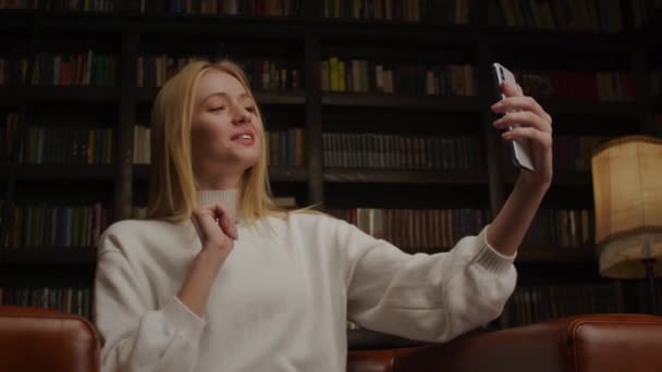 Jonge blonde vrouw glimlachen tijdens een video chat met haar vrienden online binnen — Stockvideo