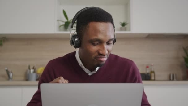 Joven agente de ventas afroamericano celebra una venta con auriculares y un portátil en frente — Vídeos de Stock