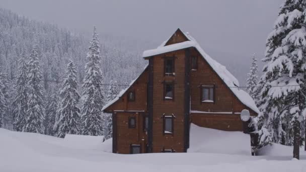 Panela sobre uma vista de paisagem de inverno em uma casa de madeira nas montanhas cobertas de neve durante a queda de neve — Vídeo de Stock