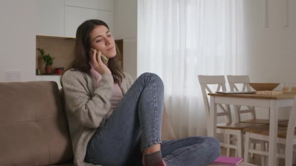 Joven morena caucásica hablando y riendo en un teléfono con amigos en un sofá en una sala de estar — Vídeos de Stock