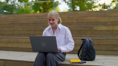 Beyaz tişörtlü mutlu genç bir kadın, açık hava ortamında dizüstü bilgisayarındaki olumlu haberlere tepki verirken sevinçle tezahürat yapıyor..