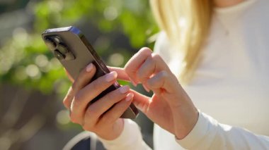 Kadınların el ele tutuşmaları ve akıllı telefonlar ile parlak doğal ışık altında etkileşim kurmaları, arka planda yeşillik olması.