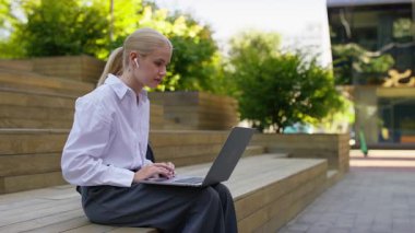 Kulaklık takan endişeli kadın, dışarıda parkta şok edici ya da üzücü haberler okuduktan sonra güvensizlik içinde dizüstü bilgisayara bakıyor..