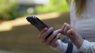 Sıradan bir şehir ortamında tek parmakla kayan akıllı telefon kullanan bir kadının ellerinin detaylı görüntüsü..