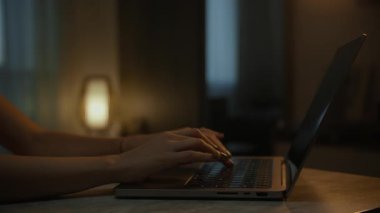 Akşamları sıcak bir odada dizüstü bilgisayarda yazı yazan eller sakin ve odaklanmış bir çalışma ortamı yaratıyor..