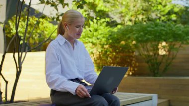 Genç profesyonel bir kadın yeşil şehir parkında çalışırken bilgisayarını video görüşmesi için kullanıyor..