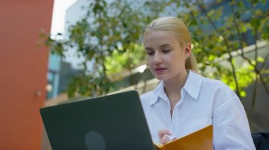 Modern şehir ortamında dizüstü bilgisayar dersini dinlerken dışarıda eğitim gören, not defterine not alan genç bir kadın..