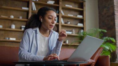 Modern ofis salonundaki dizüstü bilgisayarda gezinen odaklanmış genç iş kadını, bilgi okurken veya araştırma yaparken dikkatlice düşünüyor.