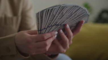 Kapalı mekanda 100 dolarlık banknotlar tutan bir kadının fotoğrafı. Nakit para, kişisel finans, tasarruf, gelir ve para yönetimi..