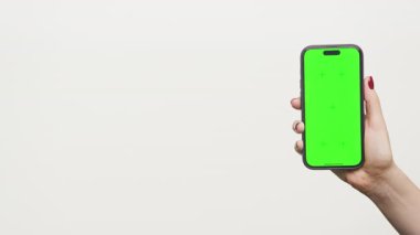 Hafif arka planda izole edilmiş yeşil ekranlı akıllı telefonu tutan kadın el, mobil uygulama modeli, reklam ve dijital sunum için ideal.