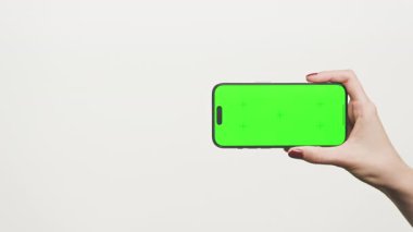 Yatay yeşil ekranlı akıllı bir telefon tutan kadın, arka planda izole edilmiş, video modeli, uygulama sunumu ve mobil reklamcılık için ideal..
