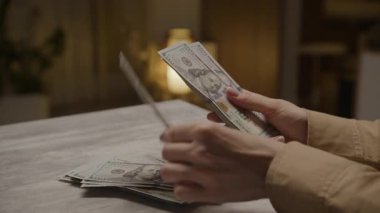 Kapalı mekan ışığında masada 100 dolarlık banknotlar sayan eller kişisel finans, bütçe ve nakit yönetimini gösteriyor..