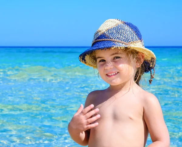 Sevimli mutlu gülümseyen küçük kız plaj tatil baş, mavi gökyüzü ve tropikal deniz arka plan üzerinde renkli şapka ile