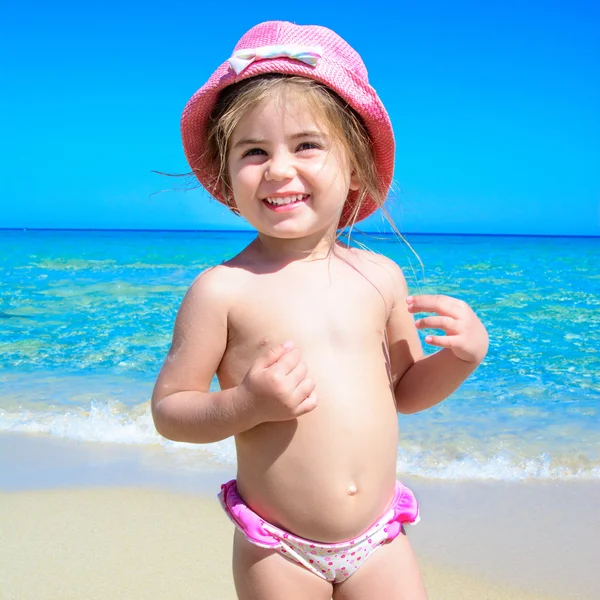 Schattig gelukkig lachend meisje op strandvakantie met kleurrijke hoed op kop, blauwe hemel en tropische zee achtergrond — Stockfoto