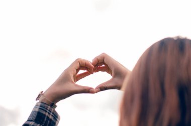 Açık mavi gökyüzüne karşı yükselen bir kalp şeklinde zafer kazanmış bir kadının eli..