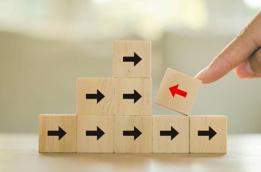 Kırmızı ok, tahta blok, iş adamının eli, ahşap masadaki siyah okun aksine onu işaret ediyor. Farklı ve benzersiz bağımsız iş fikirlerini düşünün..
