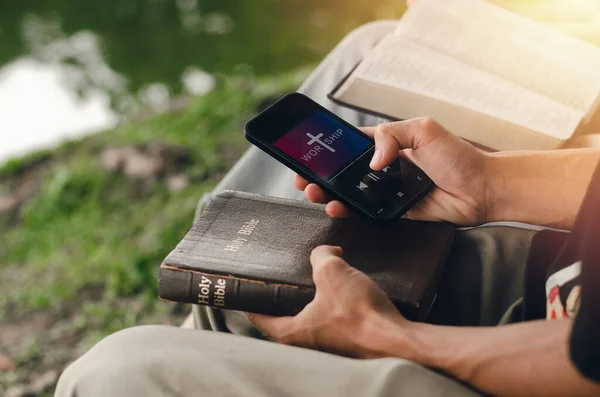 Two young people searching the Bible on their smartphones. Ready to study the Bible in the teachings of God. in the peace of nature Christian family