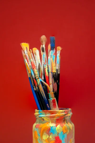 Artes pincéis de pintura em frasco de estúdio com fundo vermelho — Fotografia de Stock