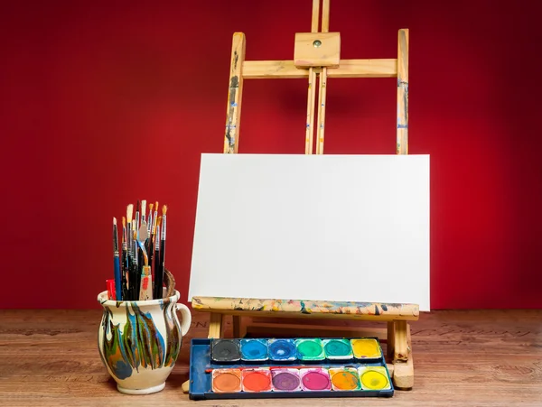 Easel palette watercolors and brushes with empty white canvas — Stock Photo, Image