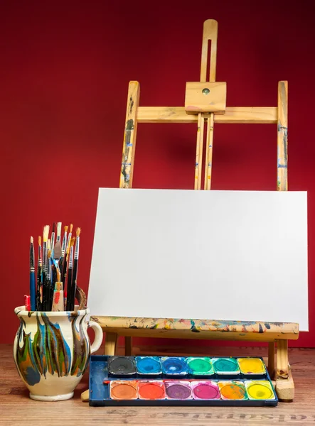 Ezel palet aquarellen en borstels met lege witte canvas — Stockfoto