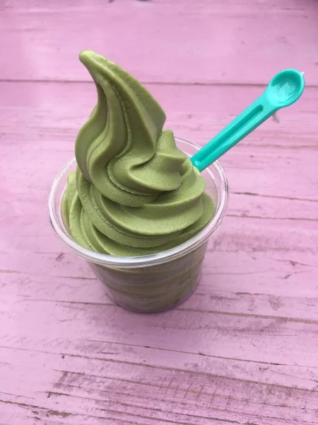 Green tea ice cream in a cup with plastic spoon on a pink table in Boseong, South Korea