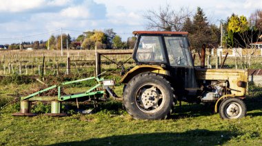 Eski, paslı, sarı traktör yeşil bir sabanla tarlada.