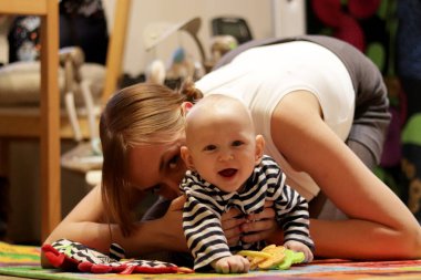 Beyaz ve gri giyinmiş beyaz kadın gülüp duran bebeğiyle sarılıyor, öpüşüyor ve oynuyor.