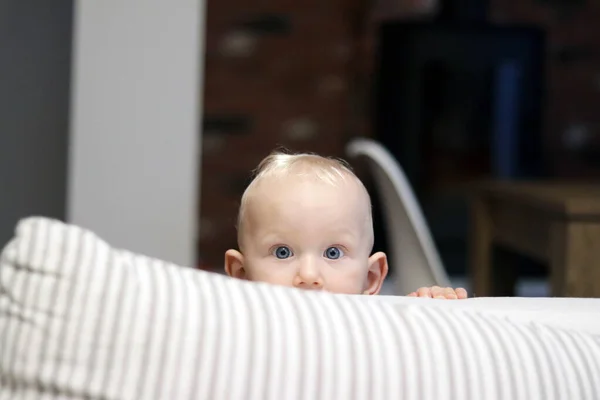 Bir çocuk yastığın arkasından şaşırmış bir yüz ifadesiyle dışarı bakıyor.