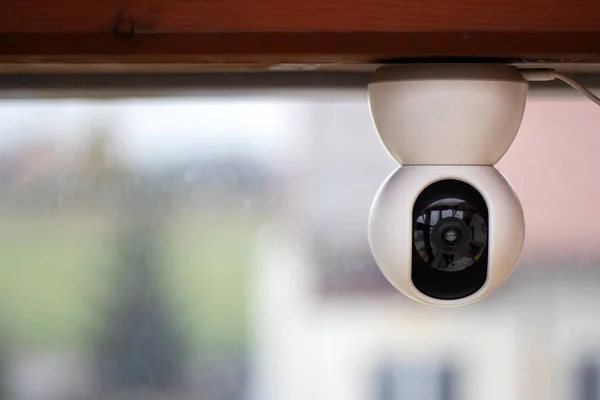 Ahşap bir kirişe baş aşağı monte edilmiş beyaz kamera. Kameraya takılı bir USB kablosu ve temiz görünen bir lensi var..