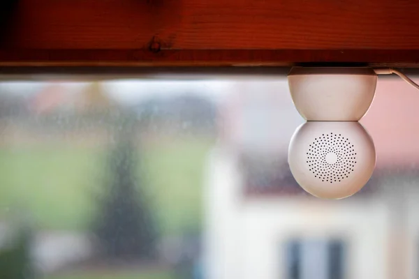 Camdan dışarı bakan ahşap bir kirişe baş aşağı monte edilmiş beyaz CCTV kamerası kameraya takılı bir USB kablosu ve sırtında desenli delikler var.