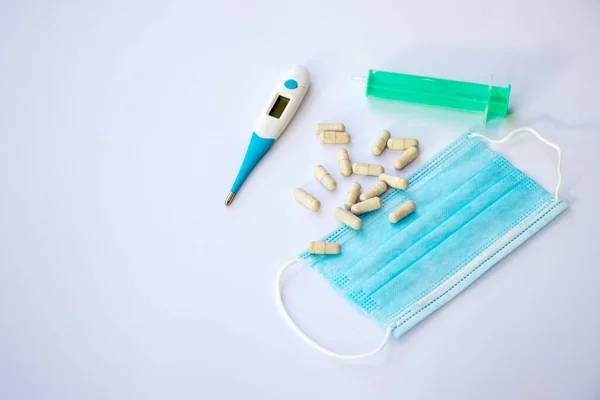 Beyaz arka planda termometre, cerrahi maske, şırınga ve haplar.