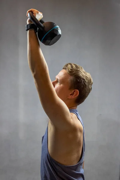 Beyaz, sarışın bir adam egzersiz yaparken elinde siyah bir kettlebell tutuyor..