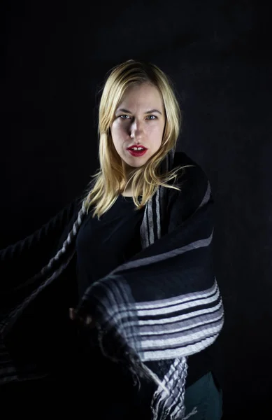 Beyaz, sarışın bir kadın elinde siyah bir eşarp ve baştan çıkarıcı bir şekilde kameraya bakıyor.