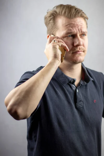 Worried, caucasian man in a black polo shirt talking on the phone. He has a golden wedding ring on his finger.