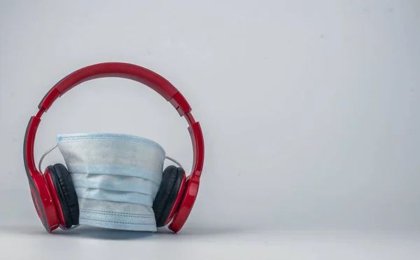 İzole edilmiş, beyaz arka planda mavi cerrahi maskeli kırmızı kablosuz kulaklıklar. Müzik, eğlence ve eğlencenin salgın sırasında bitmediğini gösteren bir konsept..
