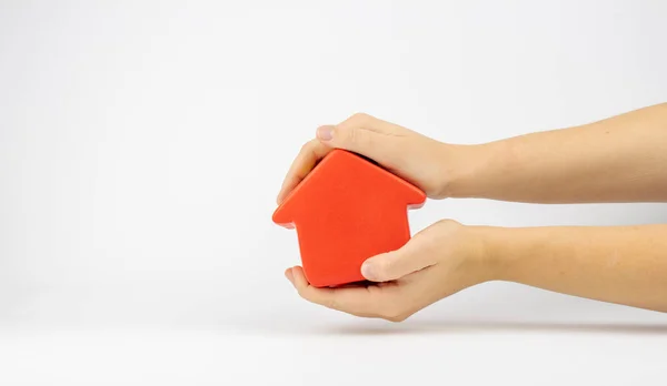 İzole edilmiş, eğimli kırmızı ev heykelciği iki elinde de beyaz bir arka planda duruyor. Bu resim, gayrimenkul alım veya satımının dürüst bir işleminin metaforudur..